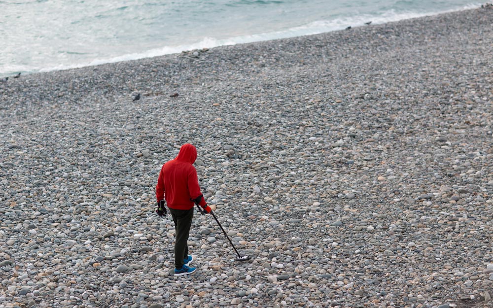 Man with a metal detector is looking for coins and jewelry on the beach